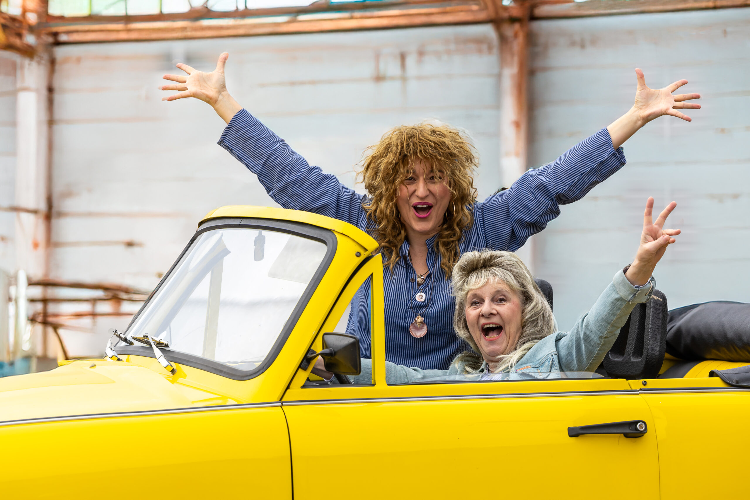 Szenenfoto: zwei Frauen reißen im gelben Trabant-Cabrio die Arme hoch