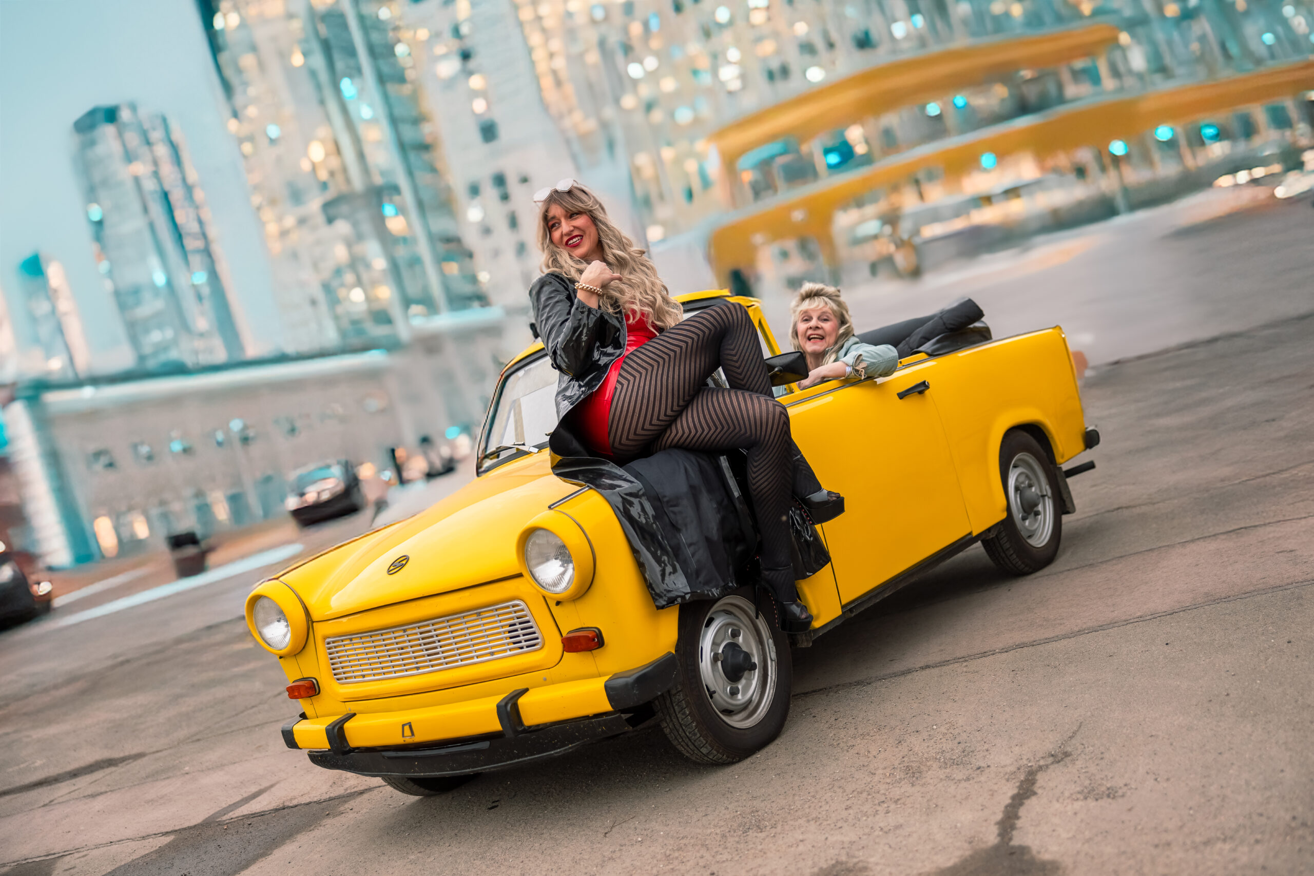 Szenenfoto: zwei Frauen in einem gelben Trabant-Cabrio vor einer Hochhauskulisse