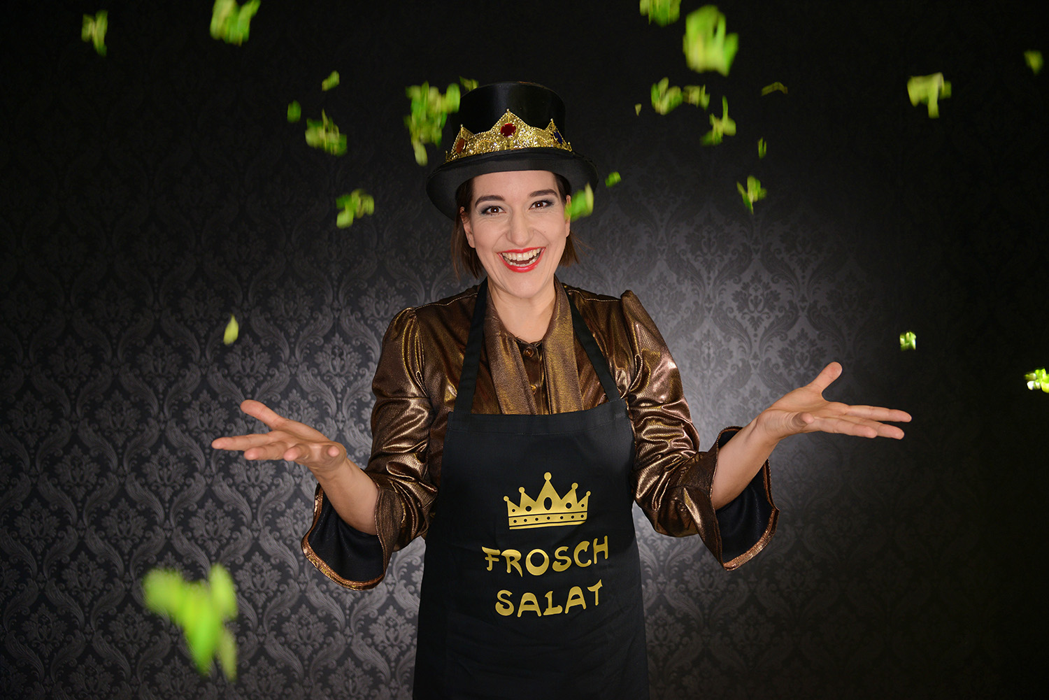 Katinka Riemann in „Froschsalat“ mit Krone und Schürze, um sie fliegen Salatblätter