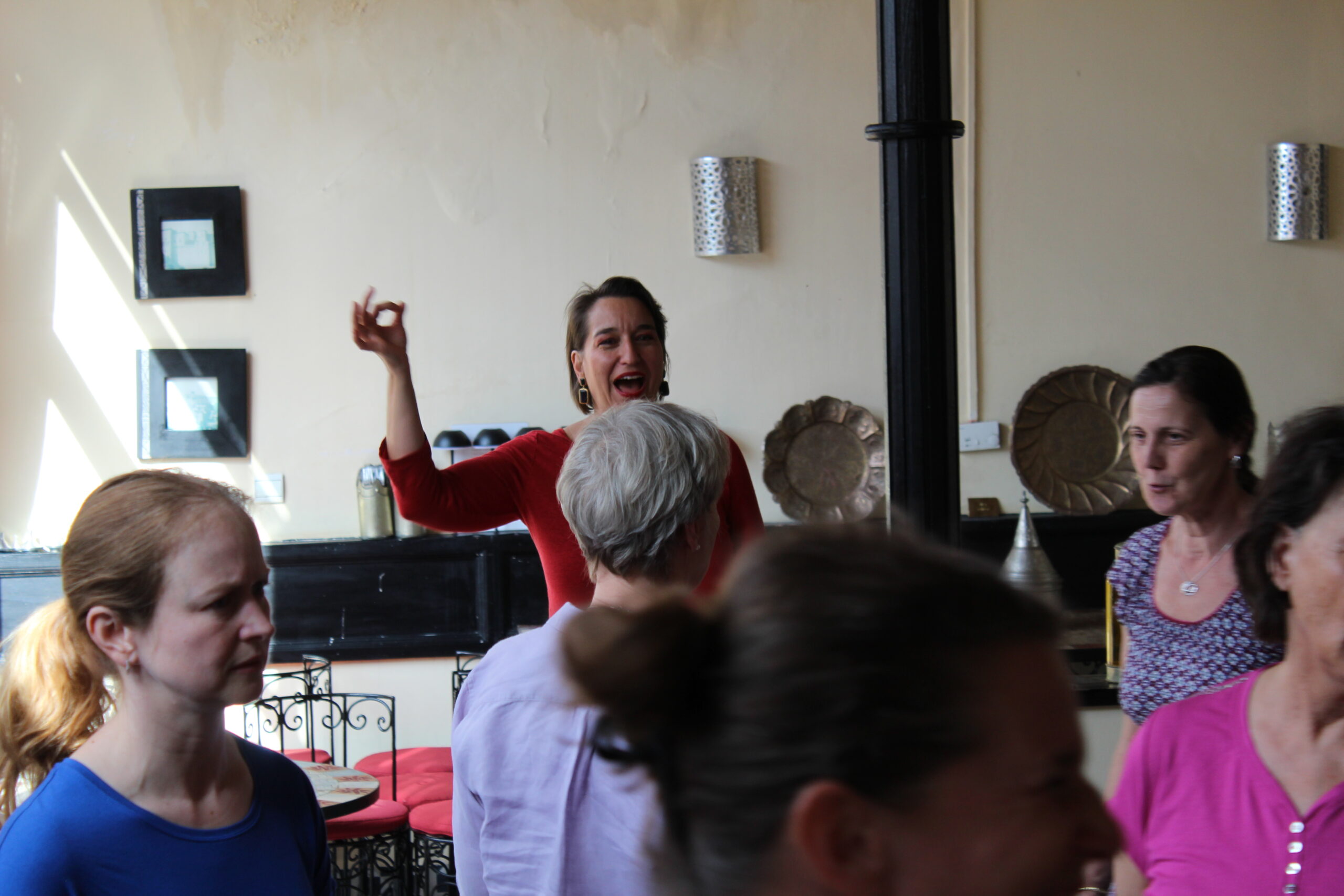 Workshop-Szene: Eine Frau in Rot hebt die Hand, Teilnehmende schauen ihr zu