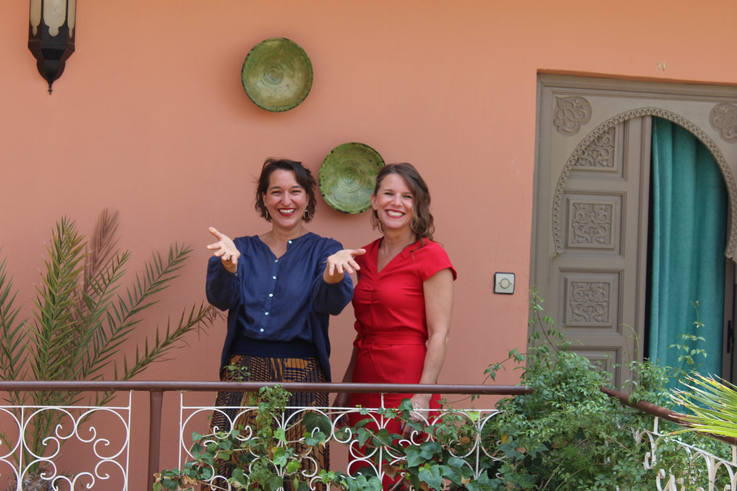 Katinka Riemann in blauer Bluse und eine Kollegin in rotem Kleid auf dem Balkon eines Riads in Marrakesch