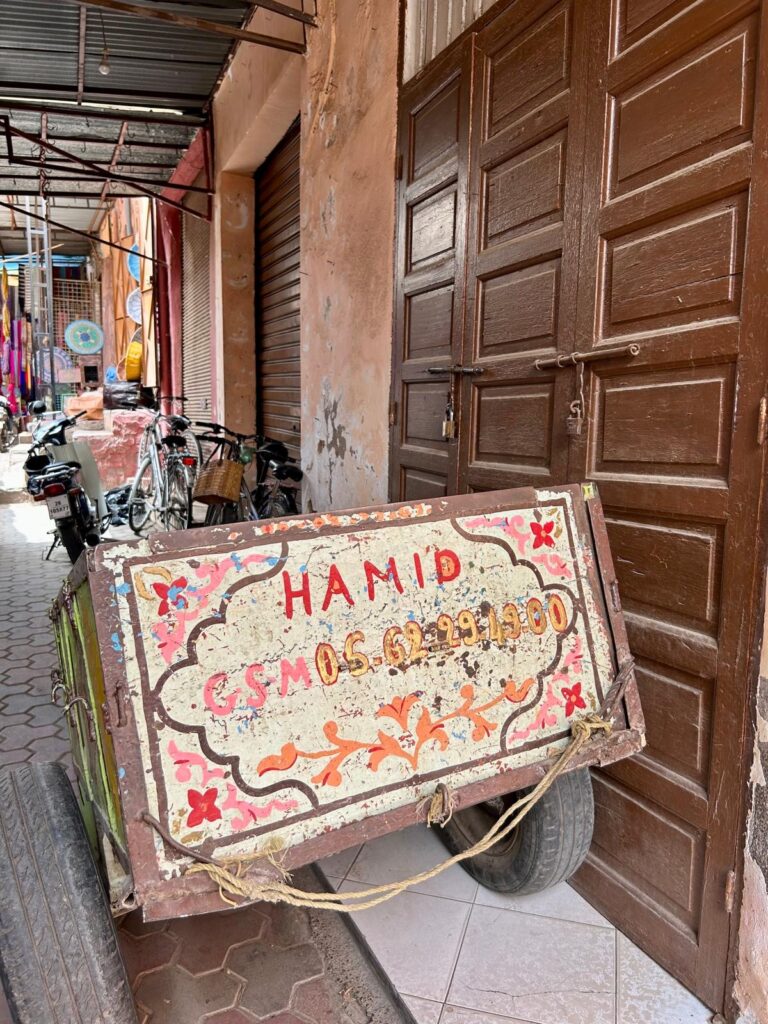 Bemaltes Holzschild „Hamid“ vor einer Holztür in einer Gasse in Marrakesch