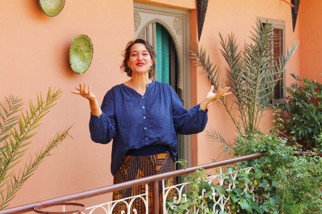 Eine Frau breitet auf einer Terrasse in Marrakesch lachend die Arme aus